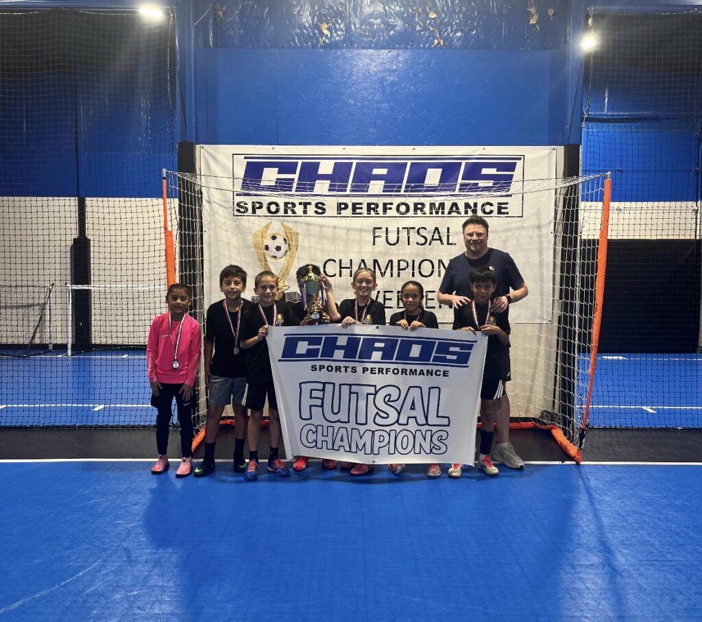 Joga Labs Black U10 futsal team with the Chaos Futsal Champions banner and trophy, Fall 2026