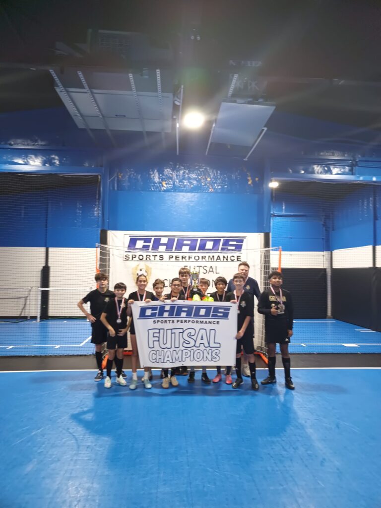 Joga Labs Black U13 futsal team with the Chaos Futsal Champions banner and trophy, Fall 2026